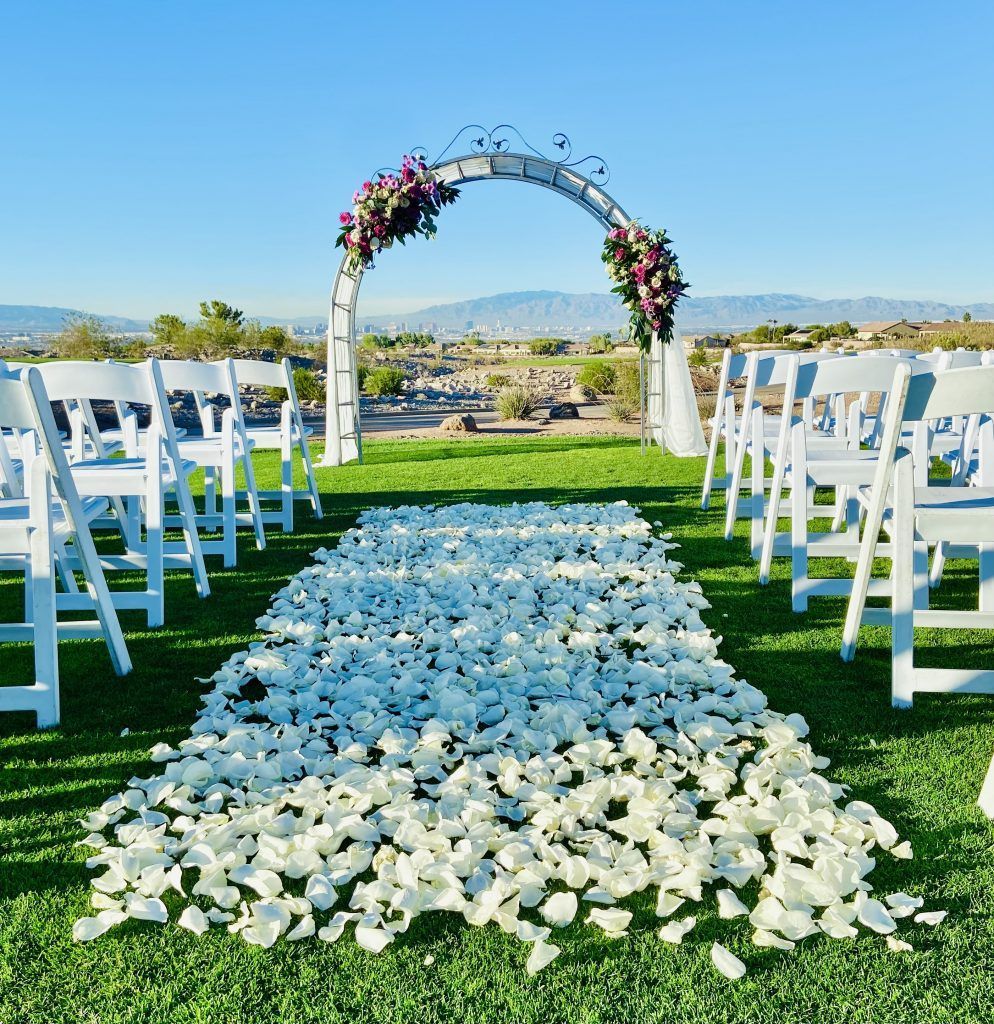 A wedding aisle with white chairs and petals on the ground