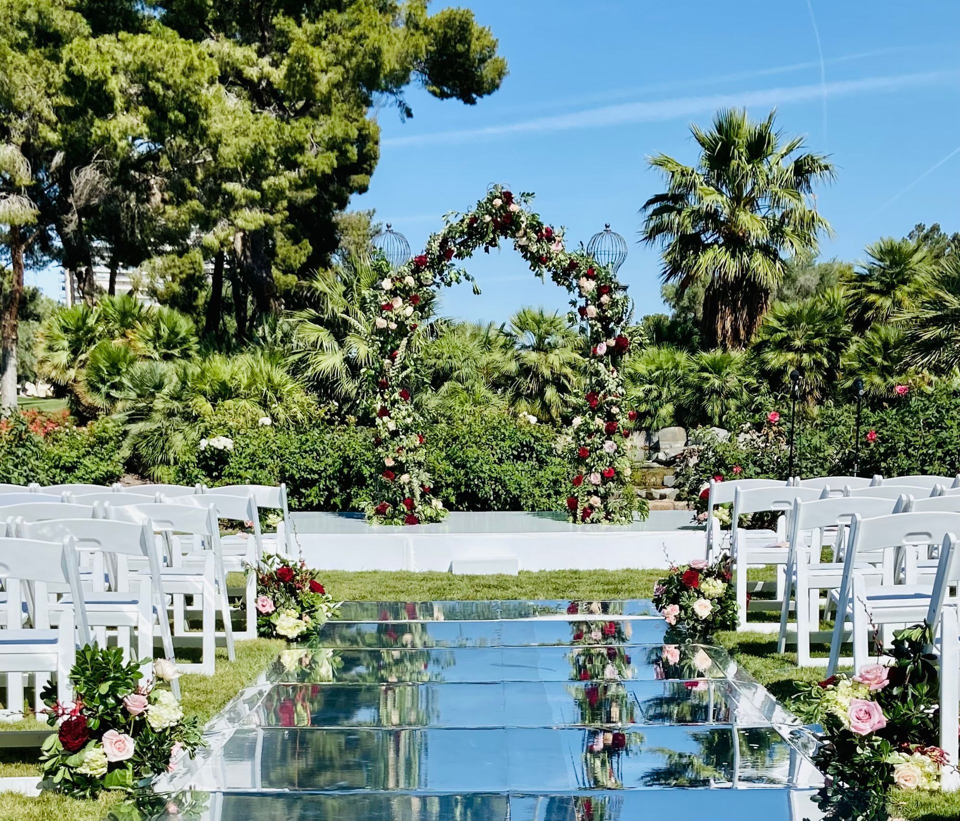 A row of white chairs are lined up in front of a floral arch.