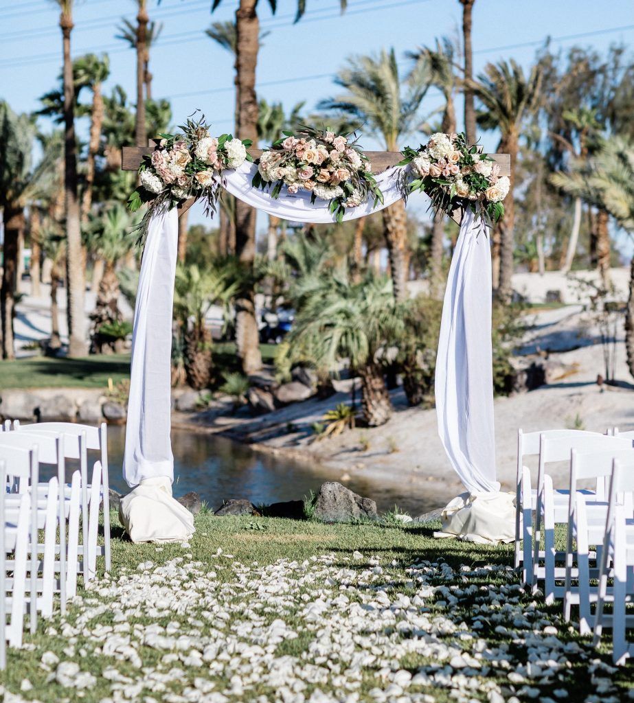 A row of white chairs are lined up in front of a floral arch.
