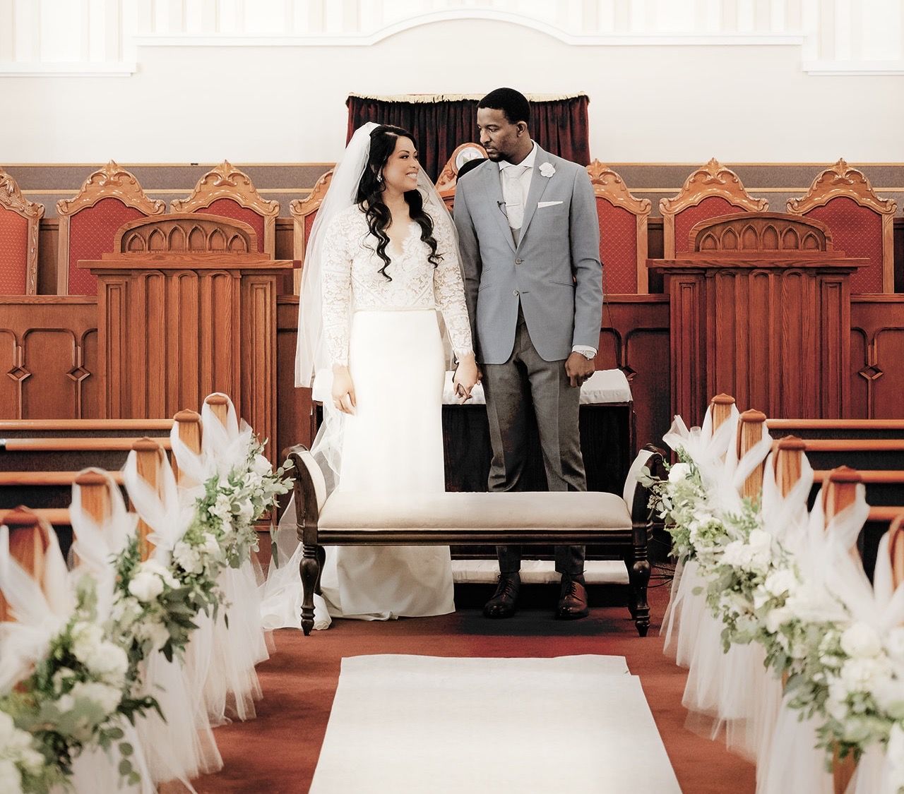 A bride and groom are standing in a church holding hands