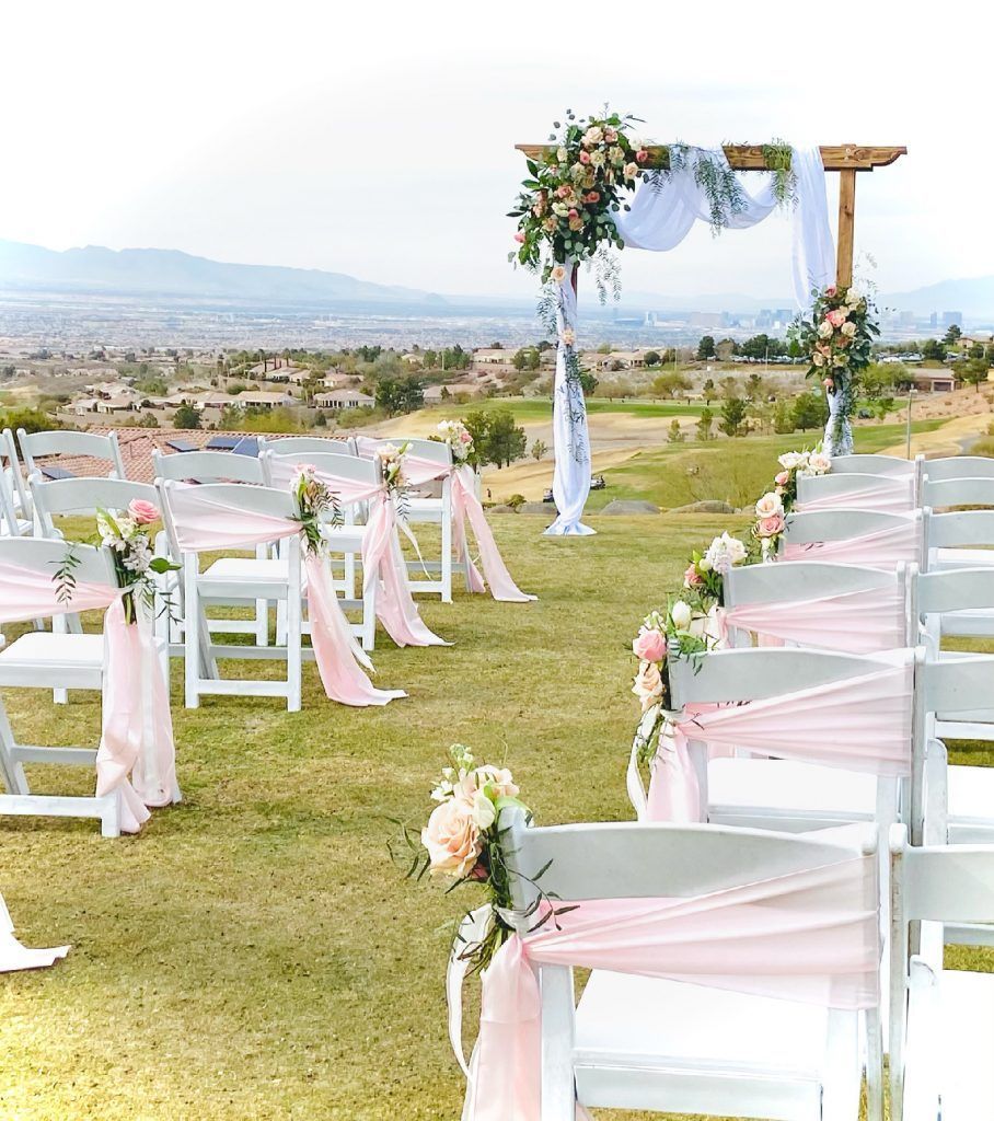 A row of white chairs decorated with pink sashes and flowers for a wedding ceremony.