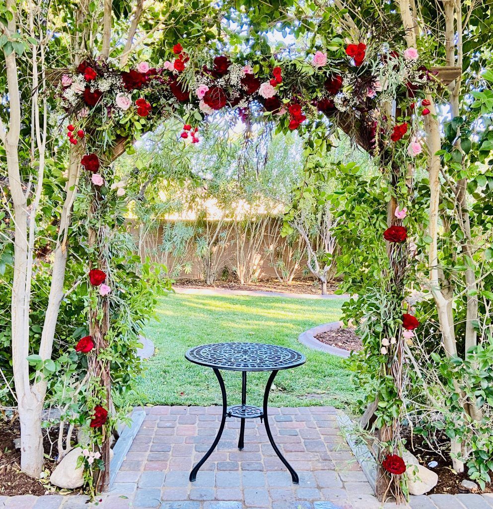 There is a table under an arch decorated with flowers.