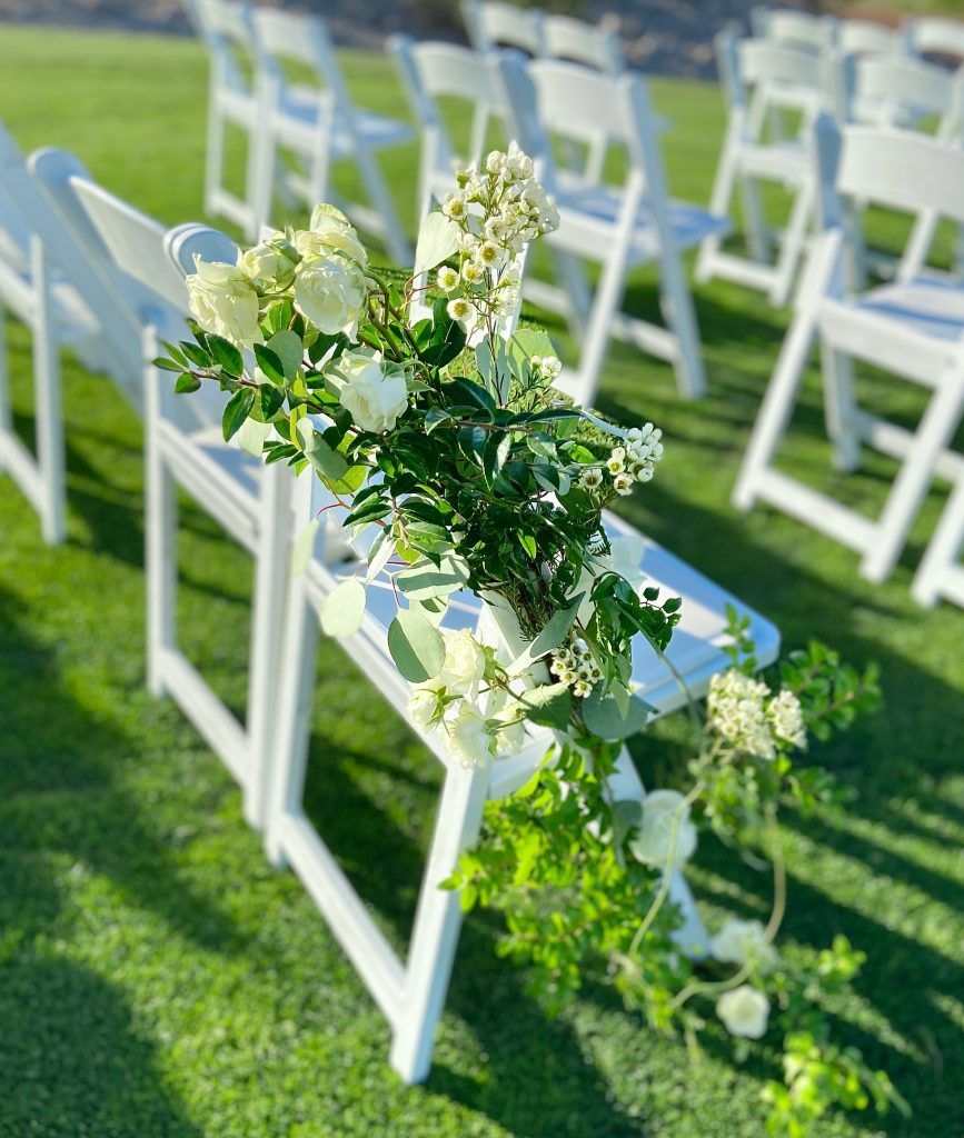 A row of white folding chairs decorated with white flowers and greenery.