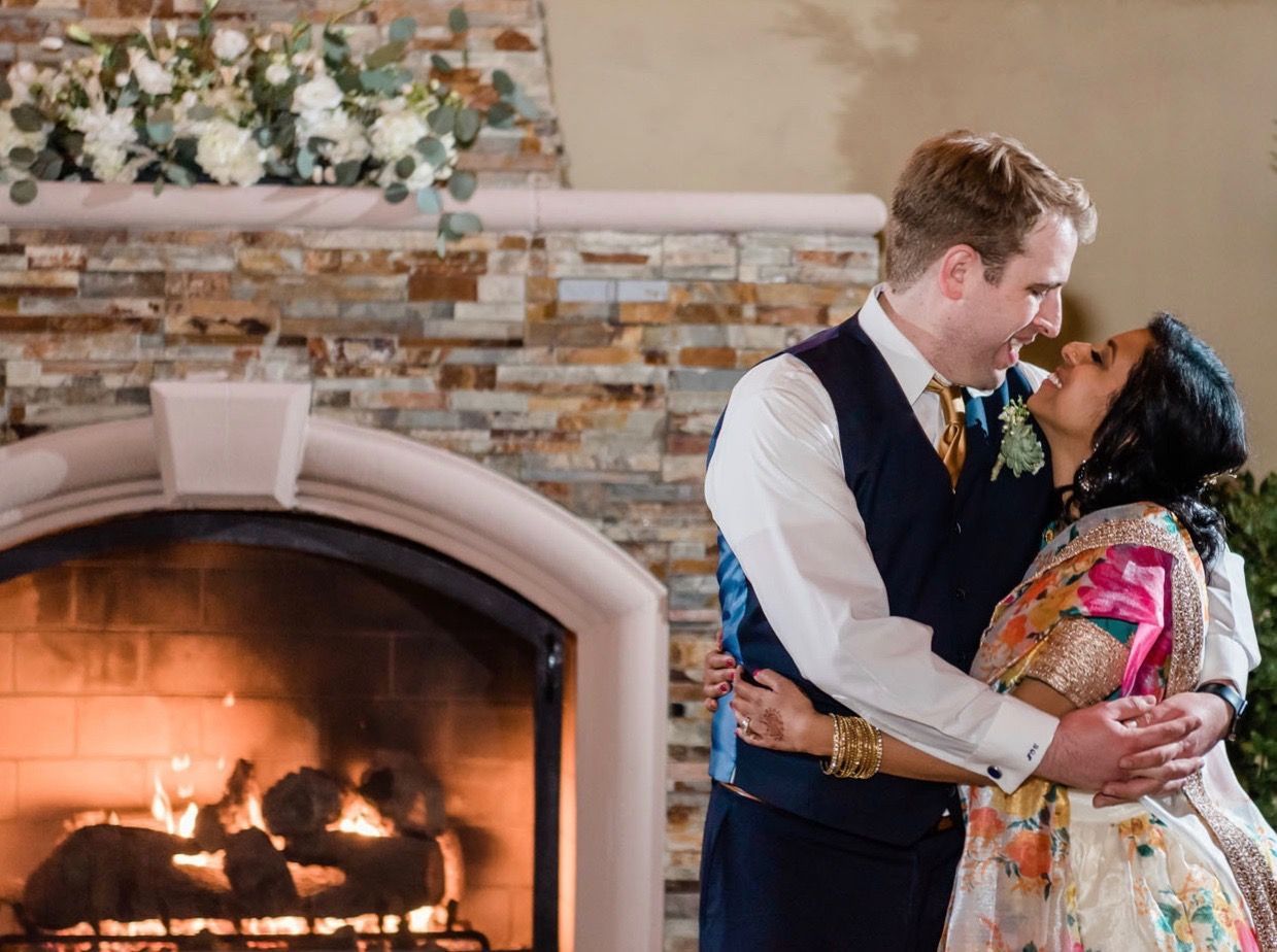 A bride and groom are dancing in front of a fireplace.