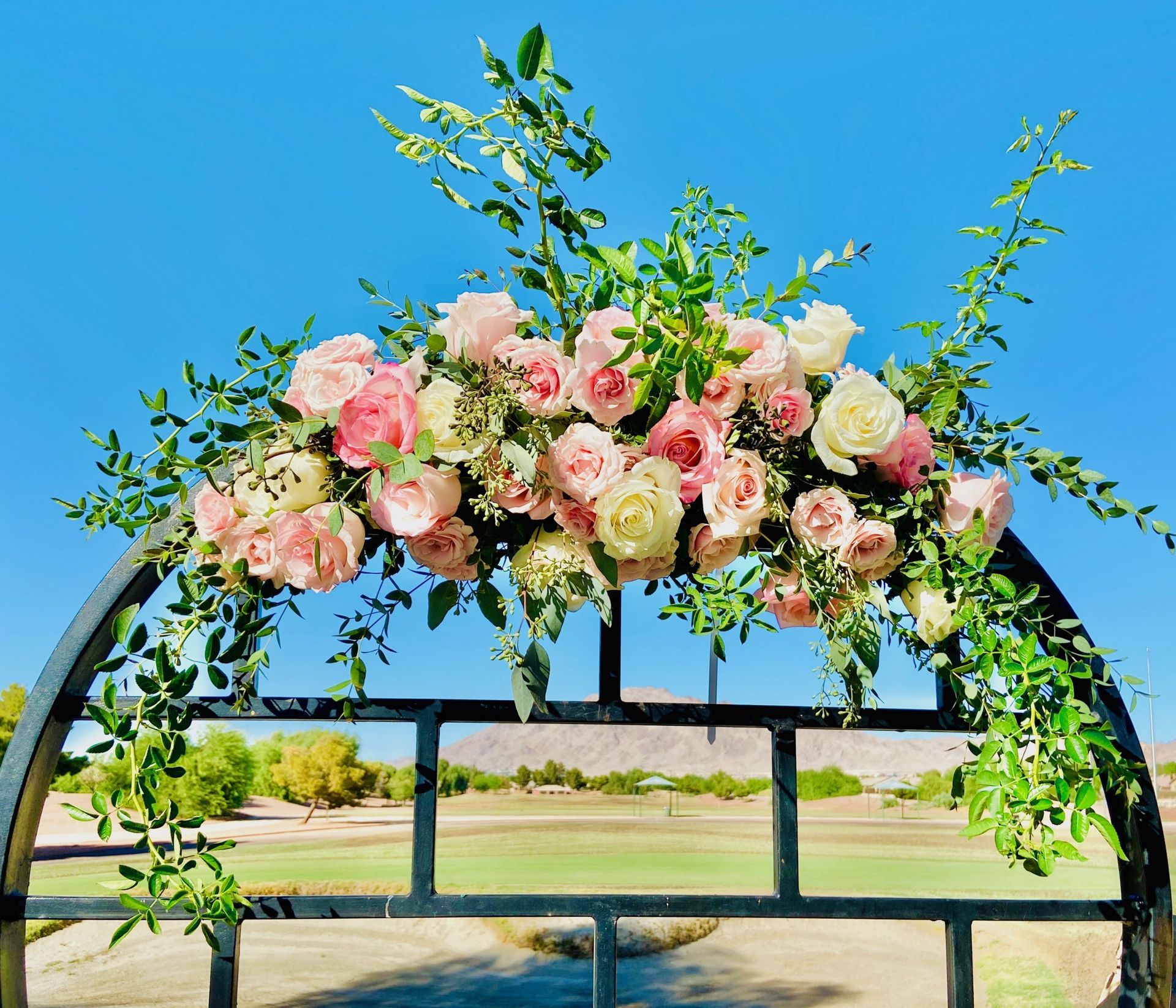 A metal arch decorated with pink and white flowers and greenery.