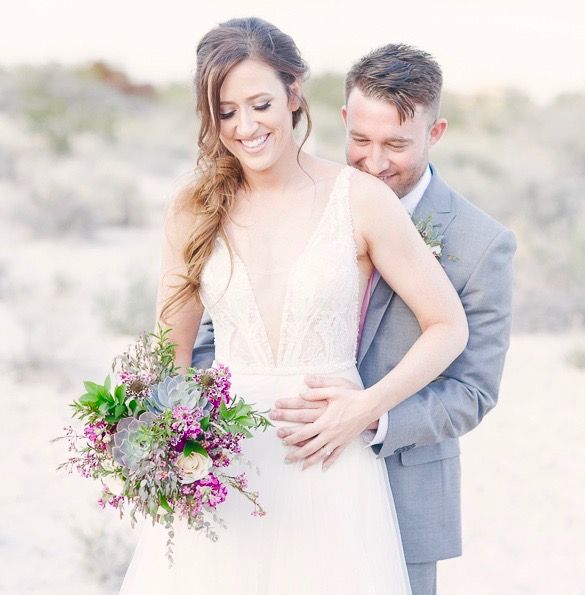 A bride and groom are posing for a picture and the bride is holding a bouquet of flowers.