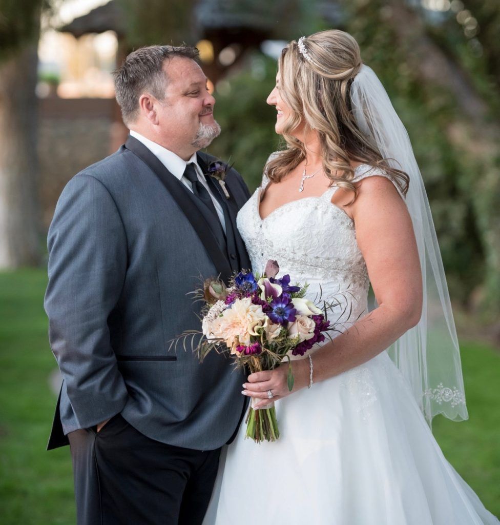 A bride and groom are standing next to each other and looking at each other.