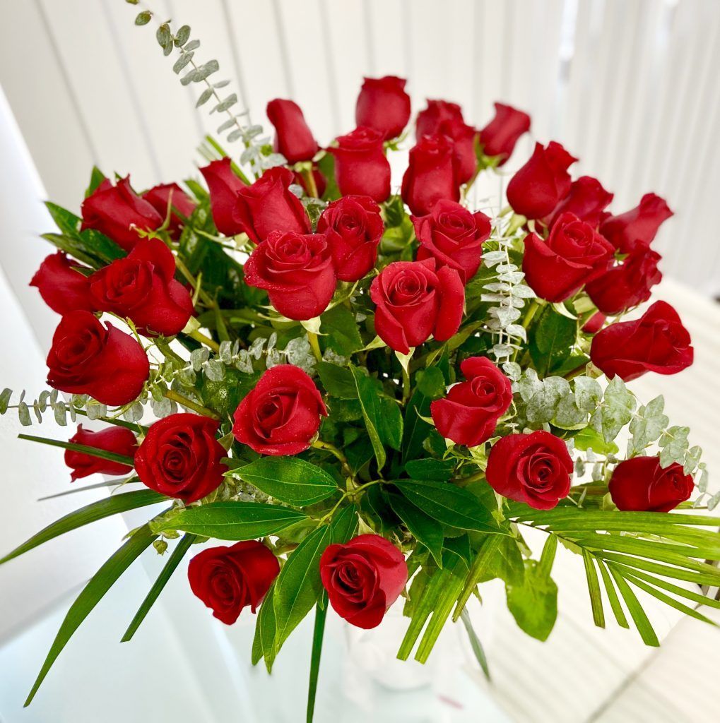 A bouquet of red roses and greenery in a vase