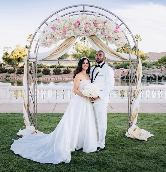 A bride and groom are posing for a picture under a floral arch.