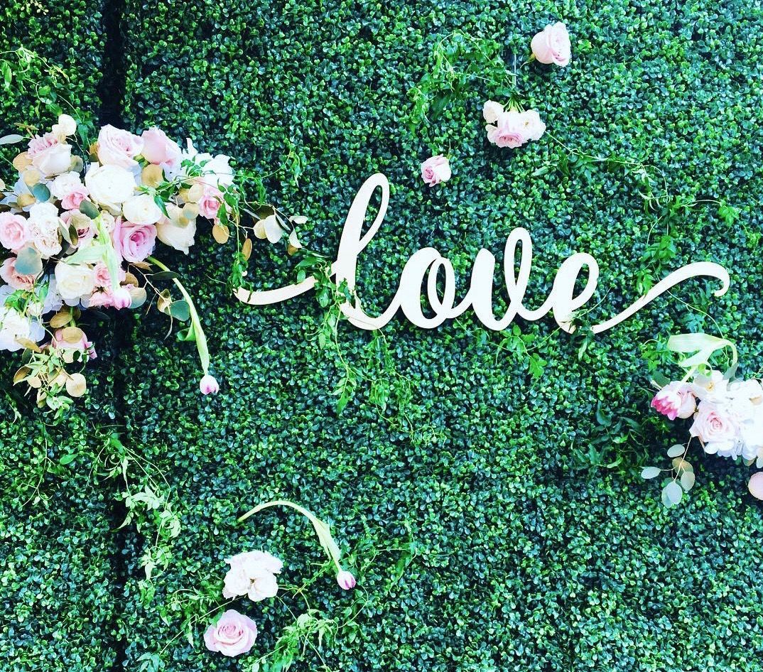 The word love is written on a green wall with flowers.