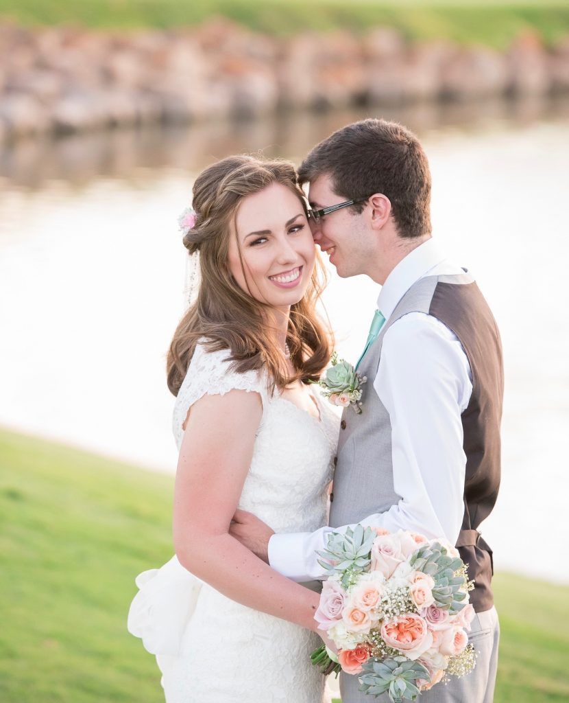 A bride and groom are posing for a picture in front of a body of water.