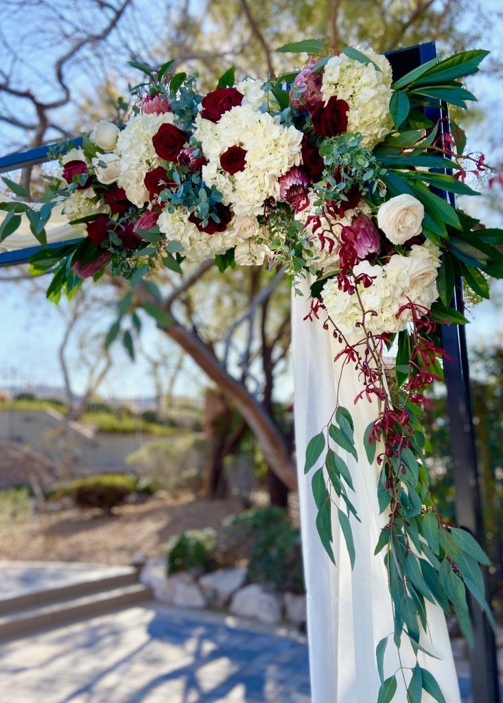 A wedding arch decorated with white and red flowers and greenery.