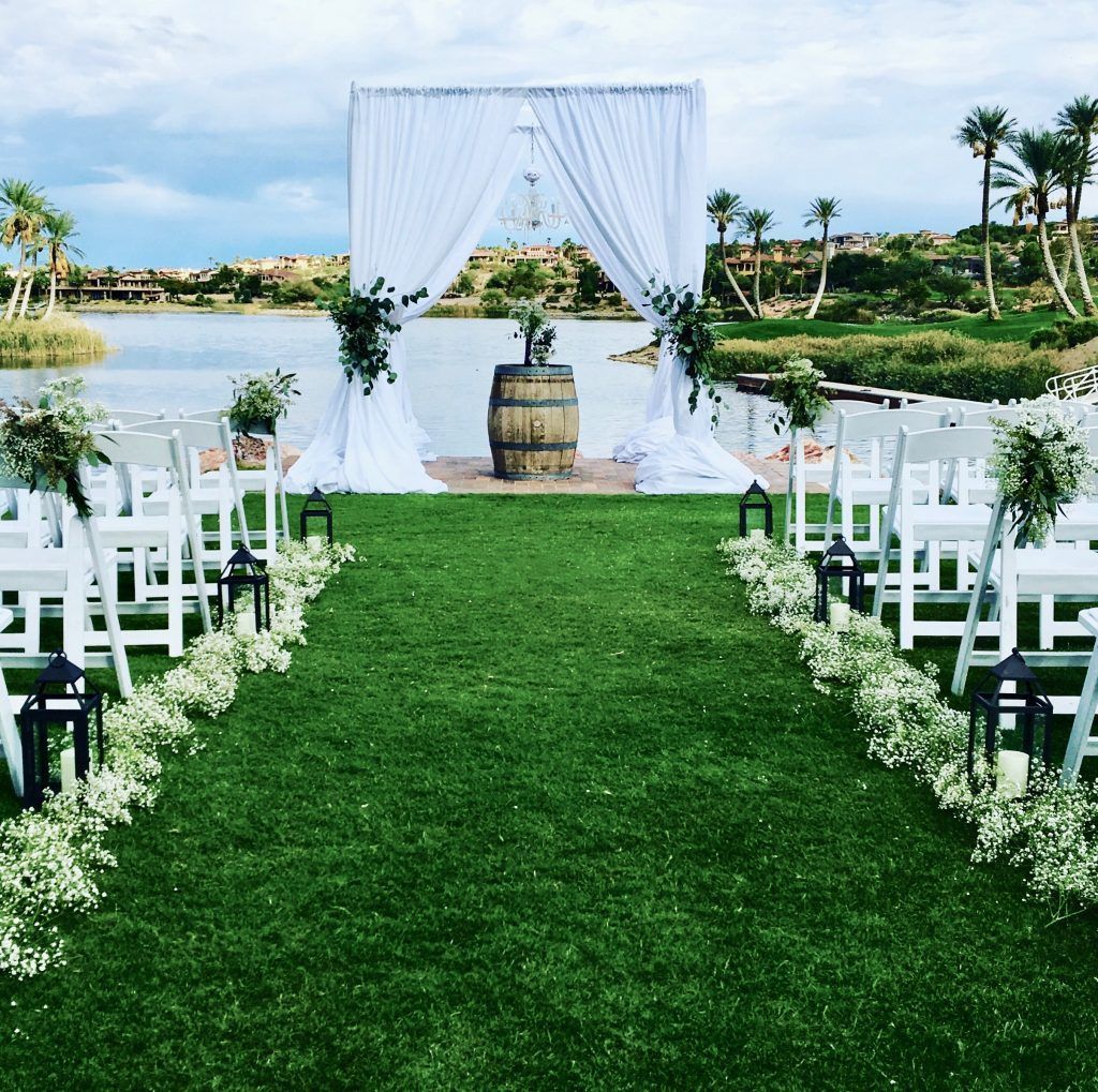 A row of white chairs are lined up in a grassy field in front of a lake.
