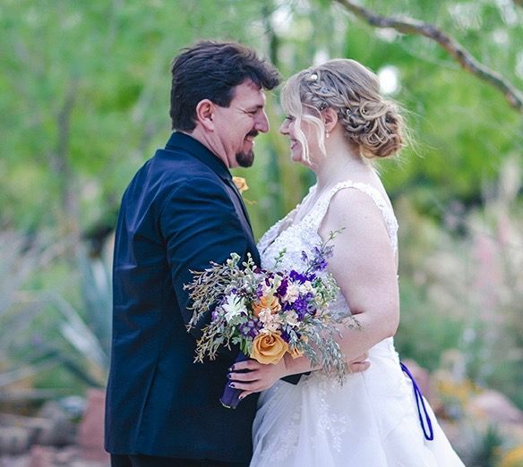A bride and groom are looking at each other while the bride is holding a bouquet of flowers.