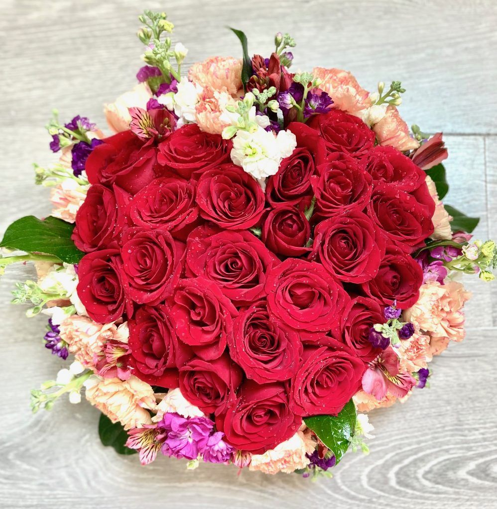 A bouquet of red roses and other flowers on a wooden table.