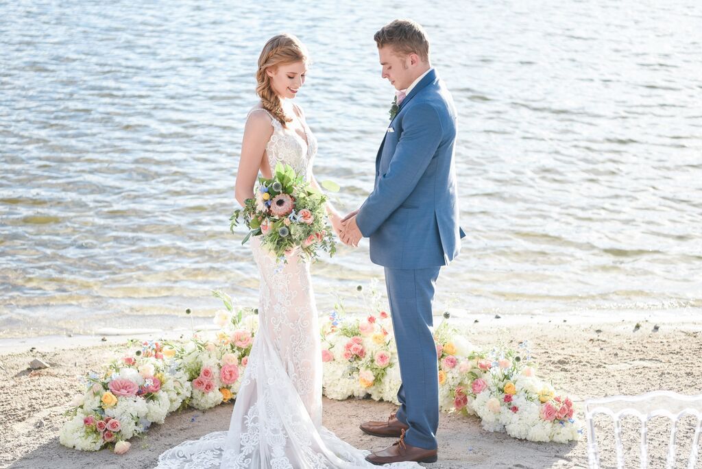 A bride and groom are holding hands on the beach.
