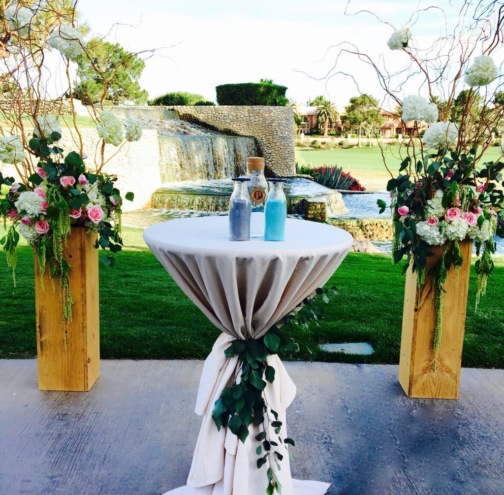 A table with two bottles of sand on it in front of a waterfall