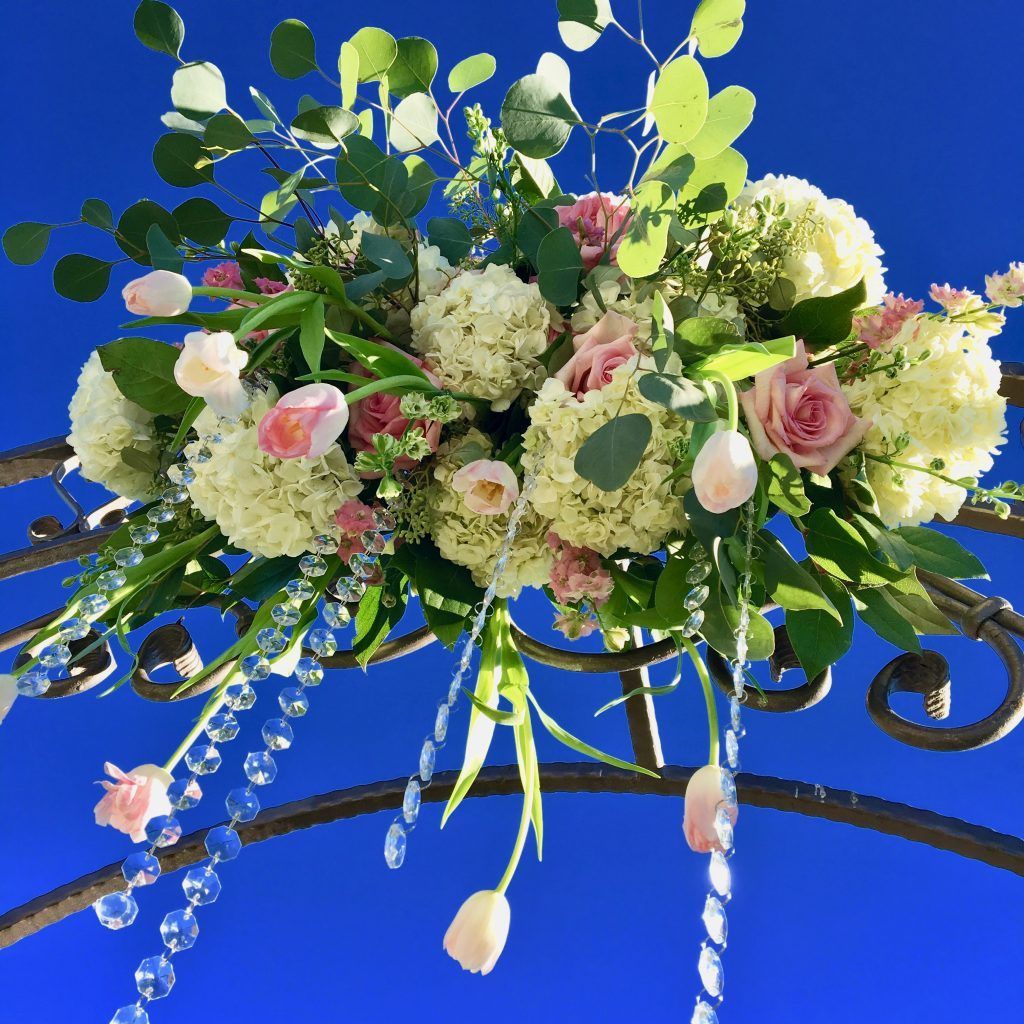 A bouquet of flowers is hanging from a wrought iron arch against a blue sky.