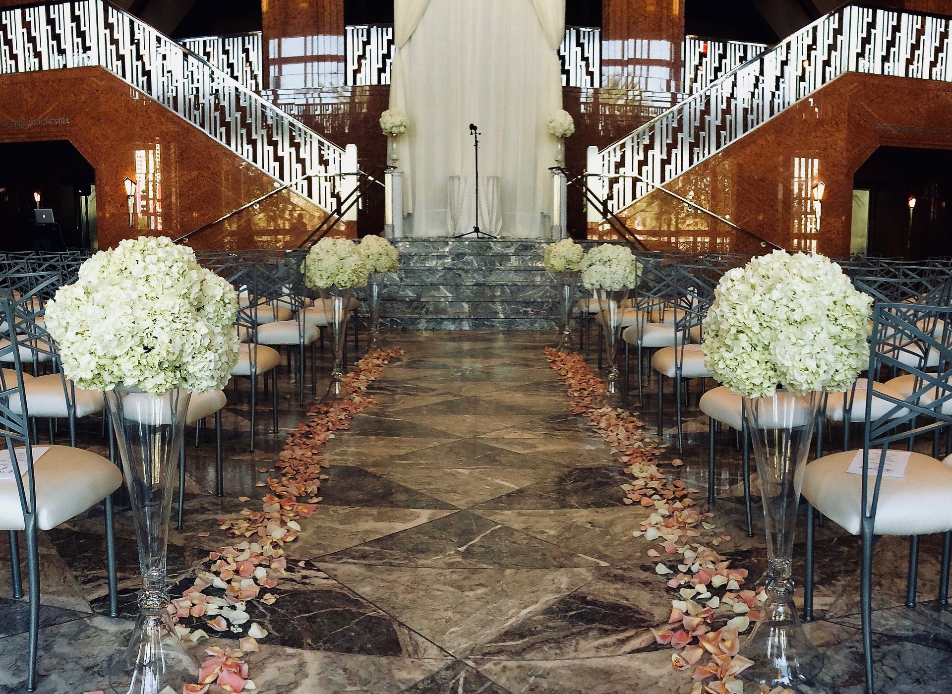 A wedding ceremony is taking place in a room with stairs and flowers on the floor.