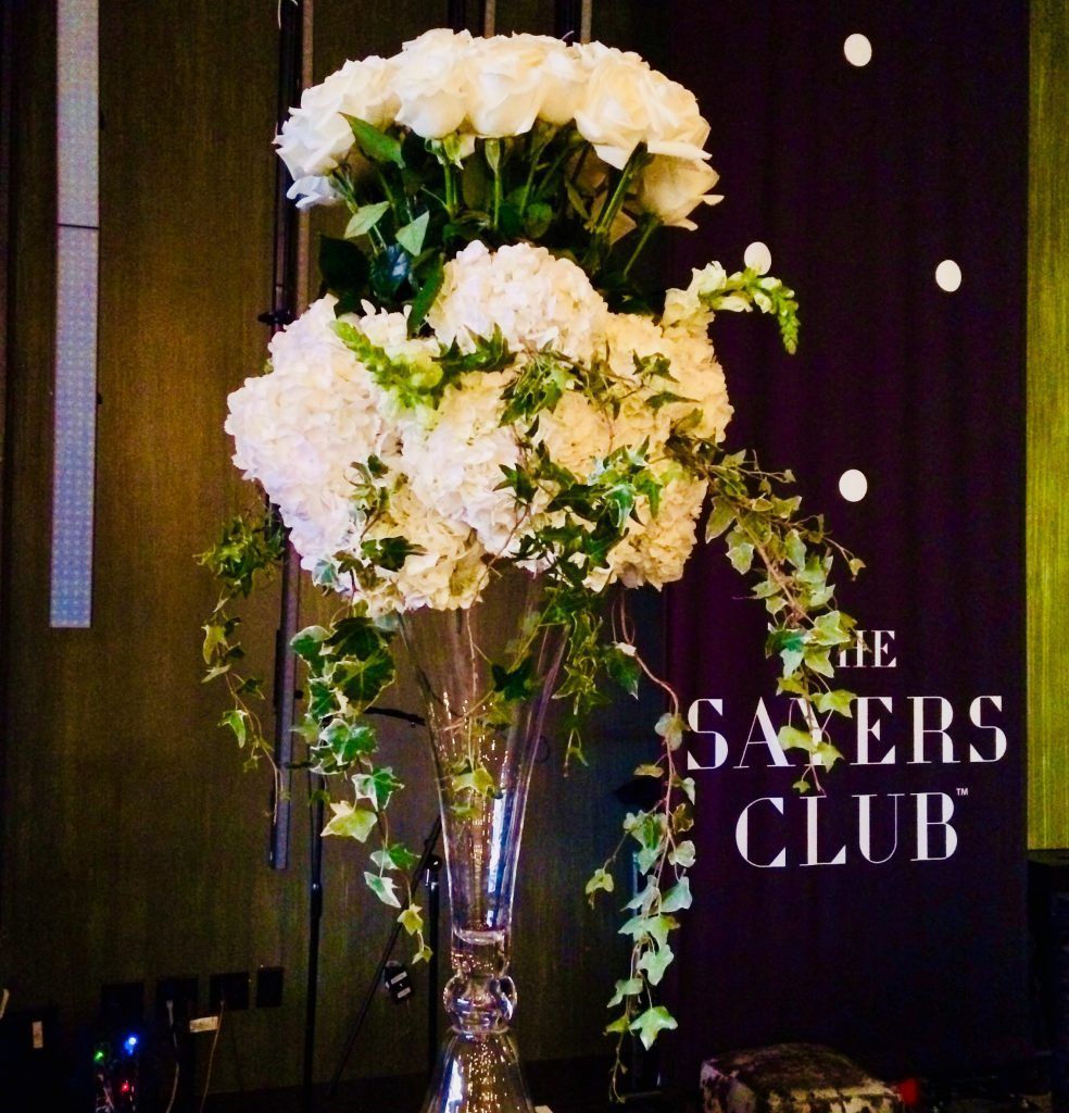 A vase of white flowers in front of a sign that says the savers club