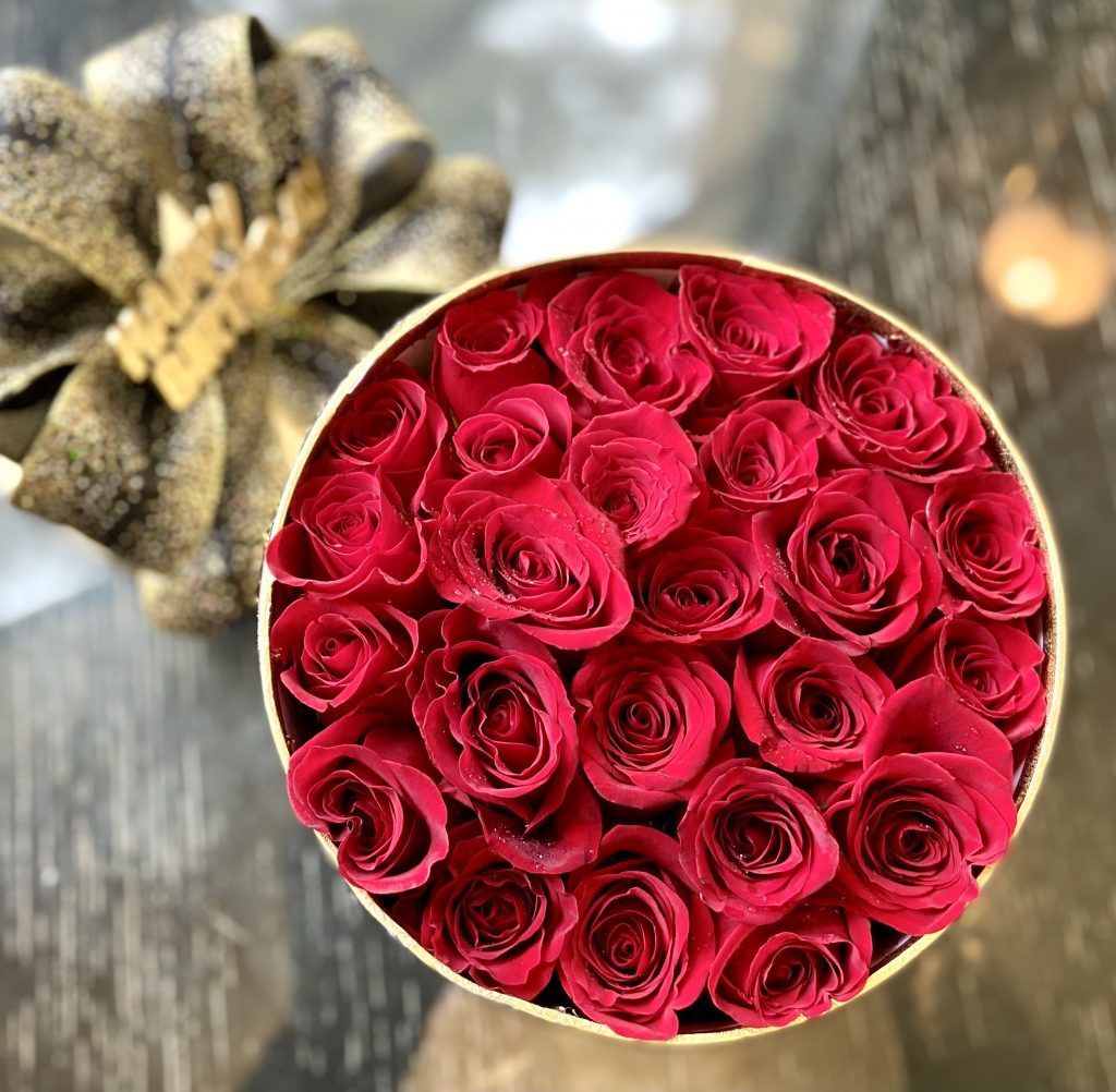 A round box filled with red roses is on a table.