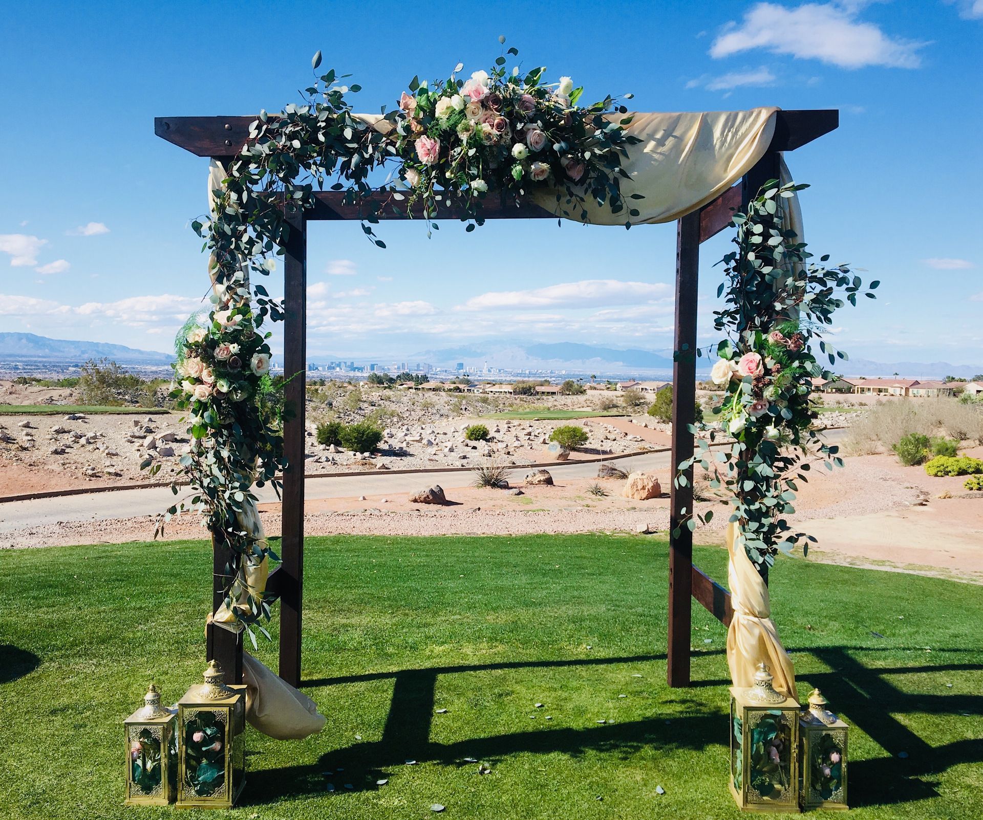 A wooden arch decorated with flowers and lanterns is sitting on top of a lush green field.
