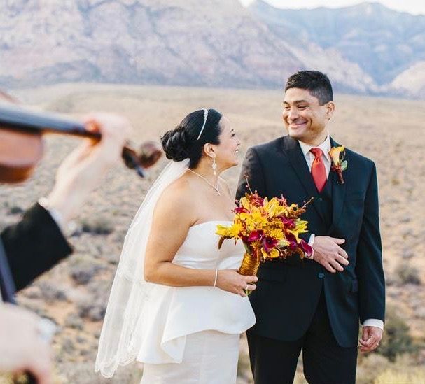 A bride and groom are posing for a picture while a man plays a violin