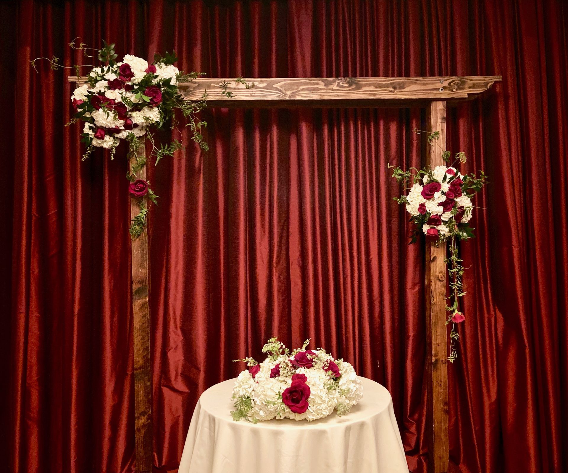 There is a table with flowers on it in front of a wooden arch.