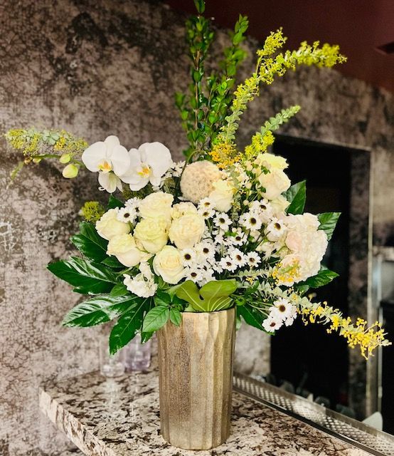 A vase filled with white and yellow flowers is sitting on a counter.