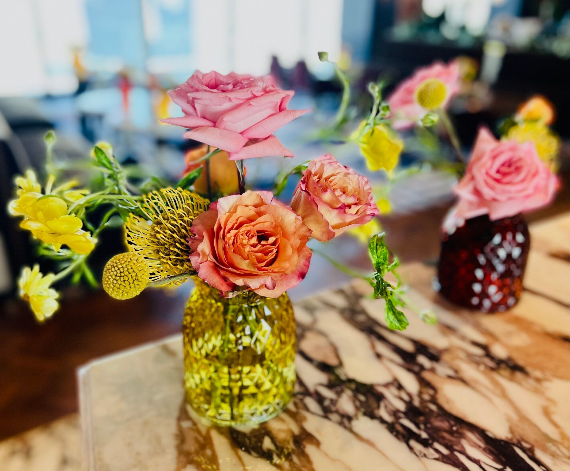 A vase filled with pink roses and yellow flowers on a table.