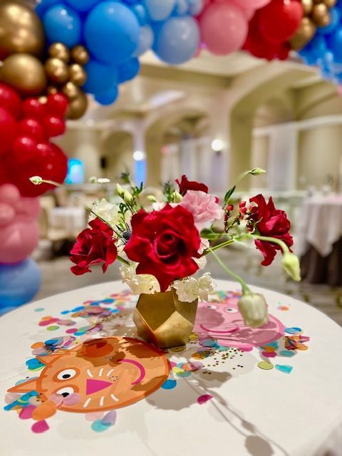 A table with a vase of flowers and balloons on it.