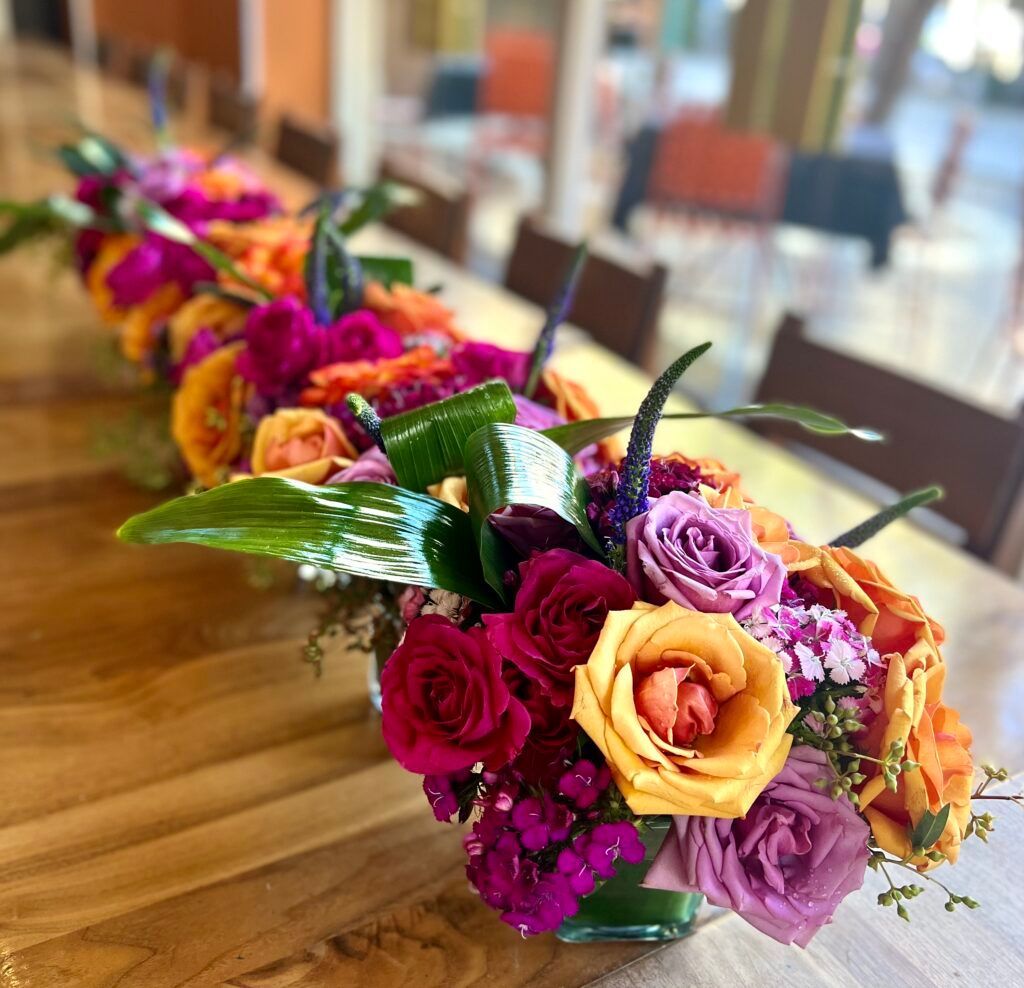 A row of vases filled with colorful flowers on a wooden table.