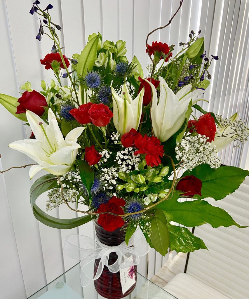 A vase filled with red , white and blue flowers on a table.