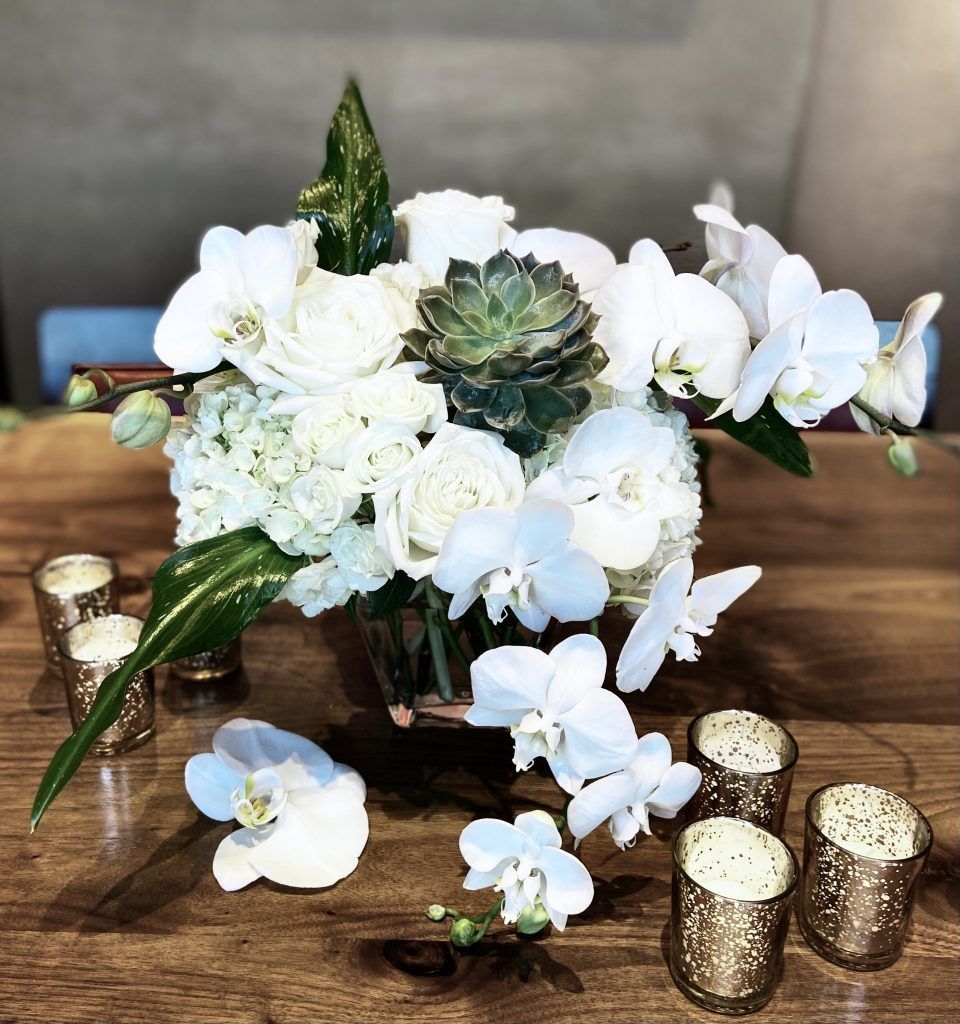 A vase filled with white flowers and candles on a wooden table.