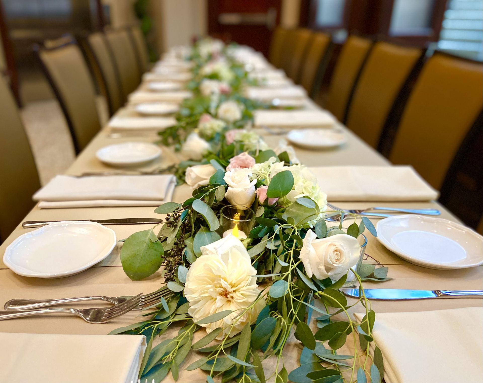 A long table with plates , silverware , and flowers on it.