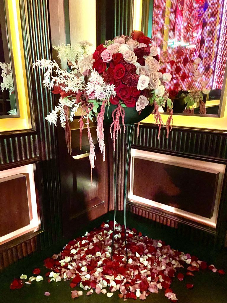 A large vase filled with red and white flowers is sitting on top of a pile of rose petals.