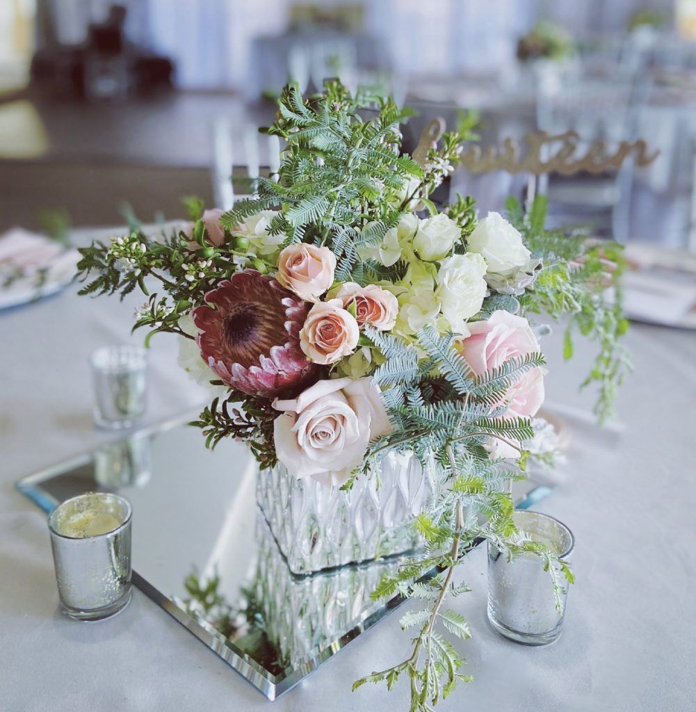 A vase of flowers is sitting on top of a mirror on a table.
