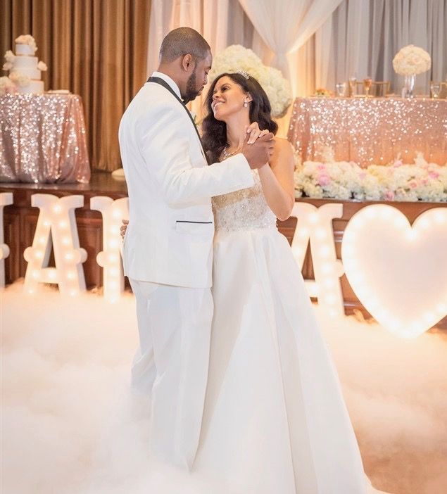 A bride and groom are dancing in front of a sign that says i love you