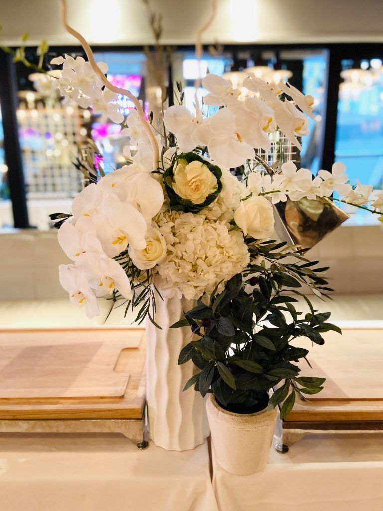 A vase filled with white flowers and potted plants on a table.