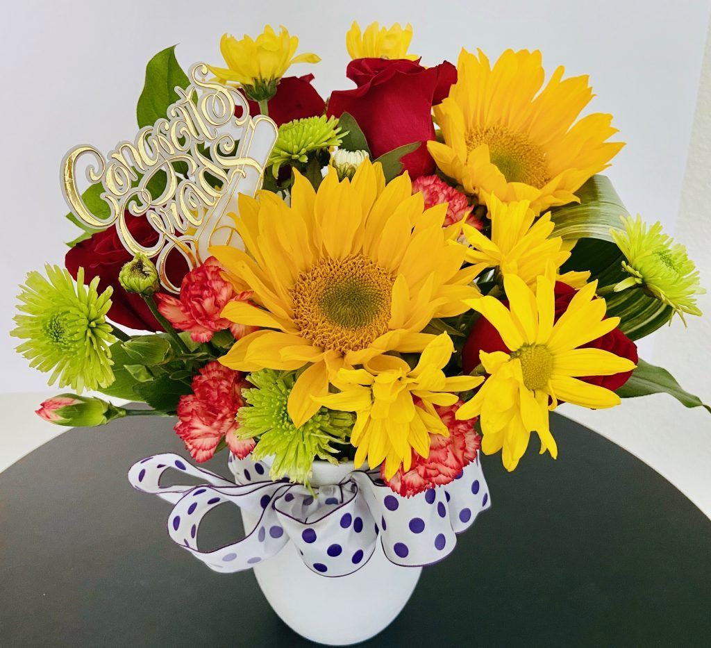 A white vase filled with yellow daisies and red roses