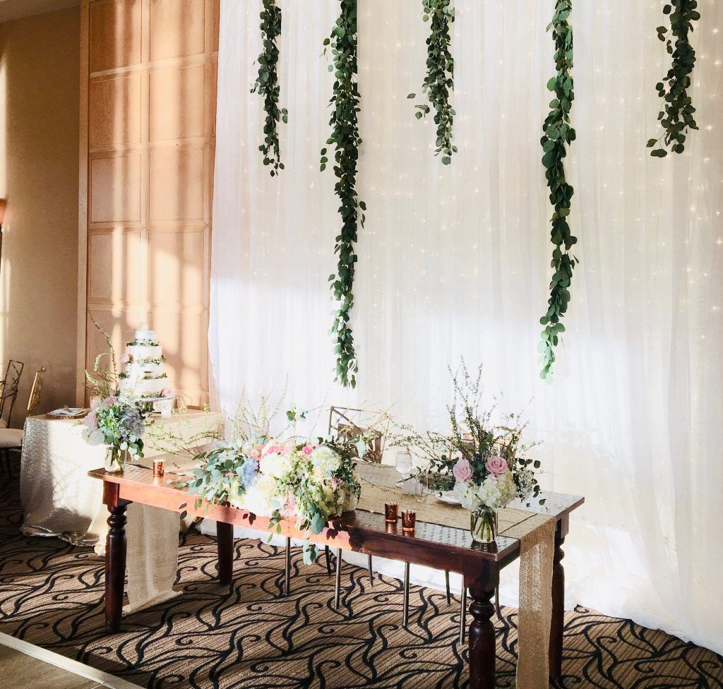 A table with flowers on it in front of a wall with ivy hanging from it.