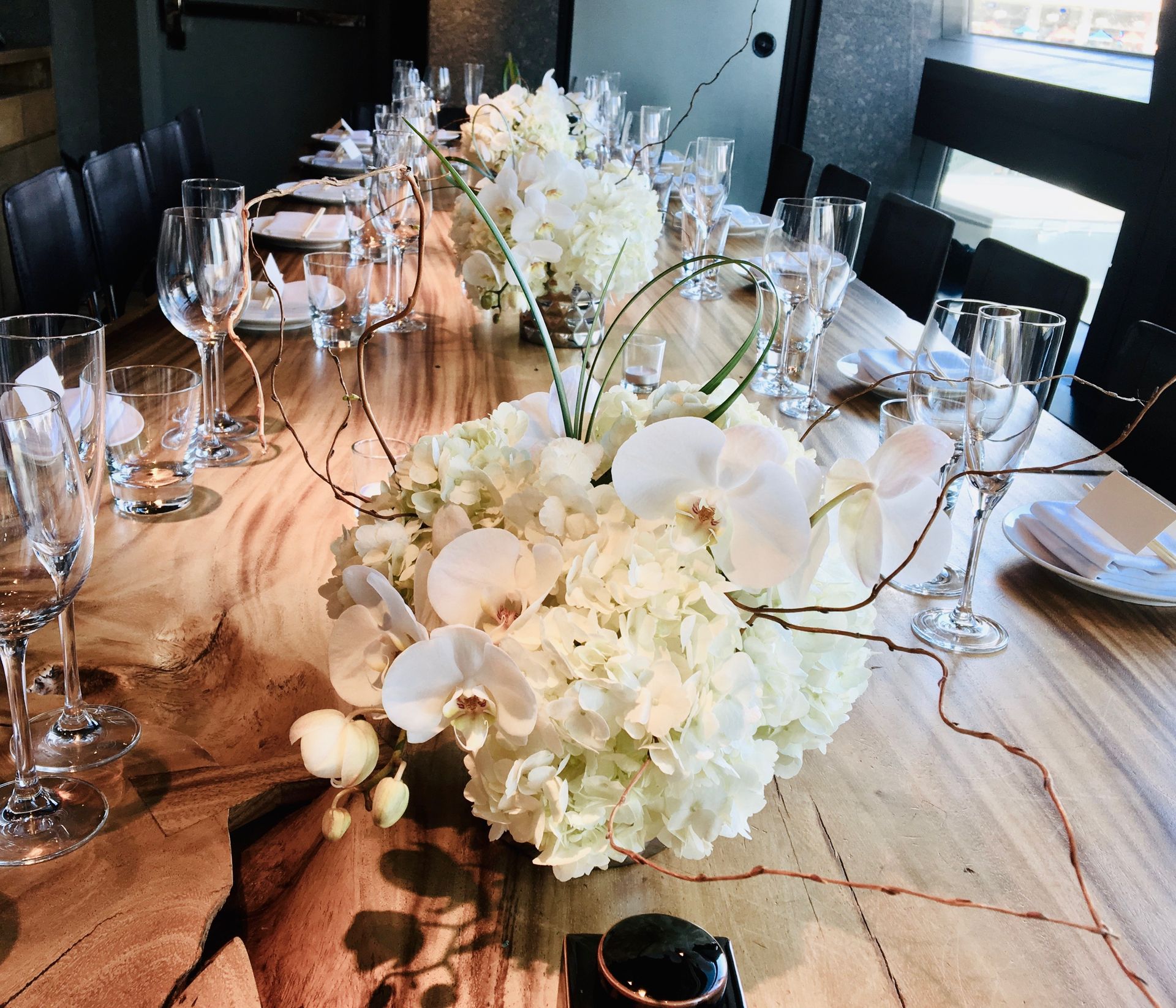 A long wooden table with flowers and wine glasses on it