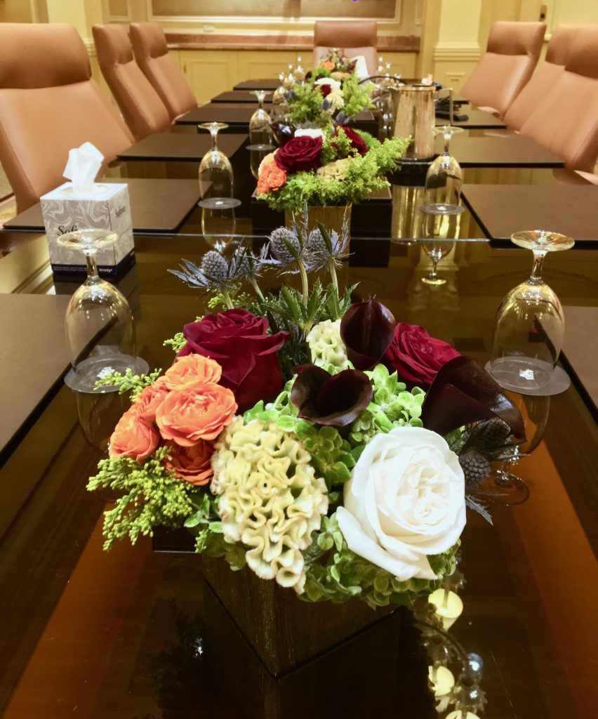 A conference table with flowers and wine glasses on it