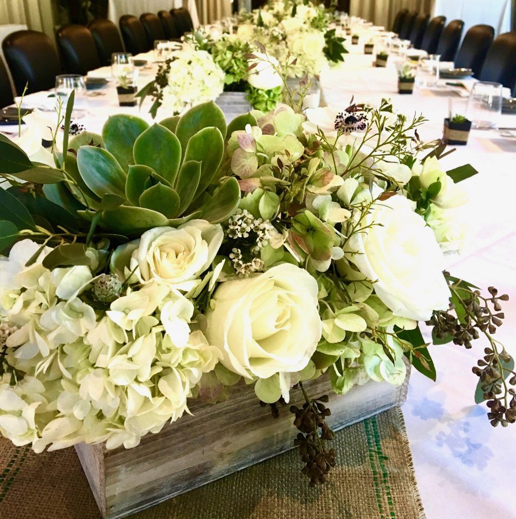 A long table with flowers and succulents on it.