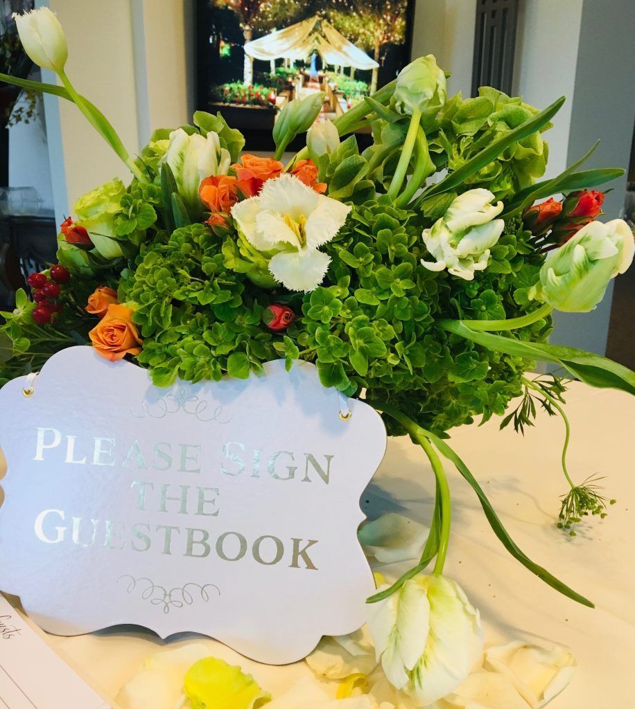 A table with flowers and a sign that says please sign the guestbook