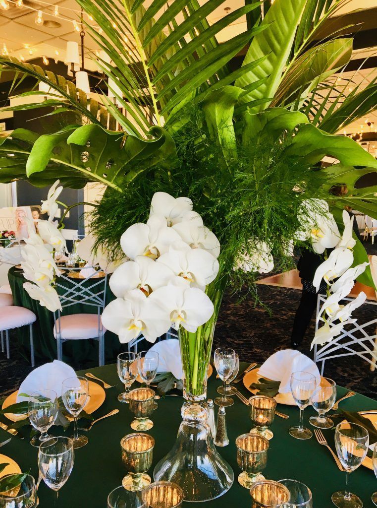 A table with a vase of white flowers and green leaves on it.