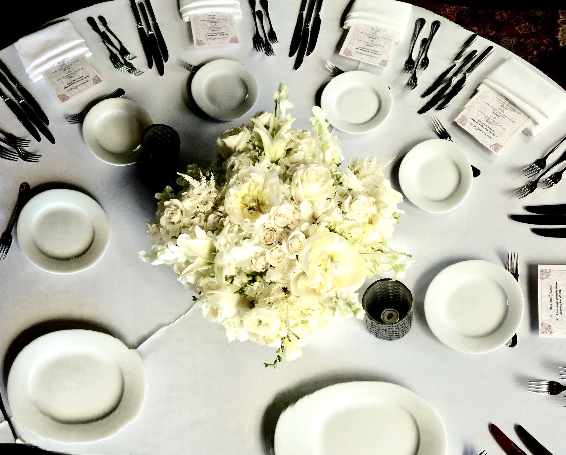 A round table with white plates and silverware and a bouquet of white flowers in the center