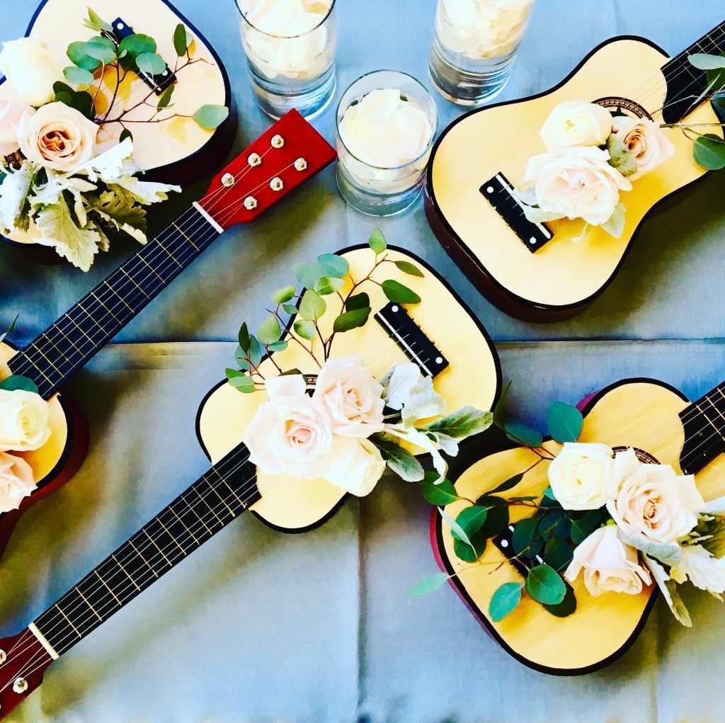 Three guitars decorated with flowers and candles on a table