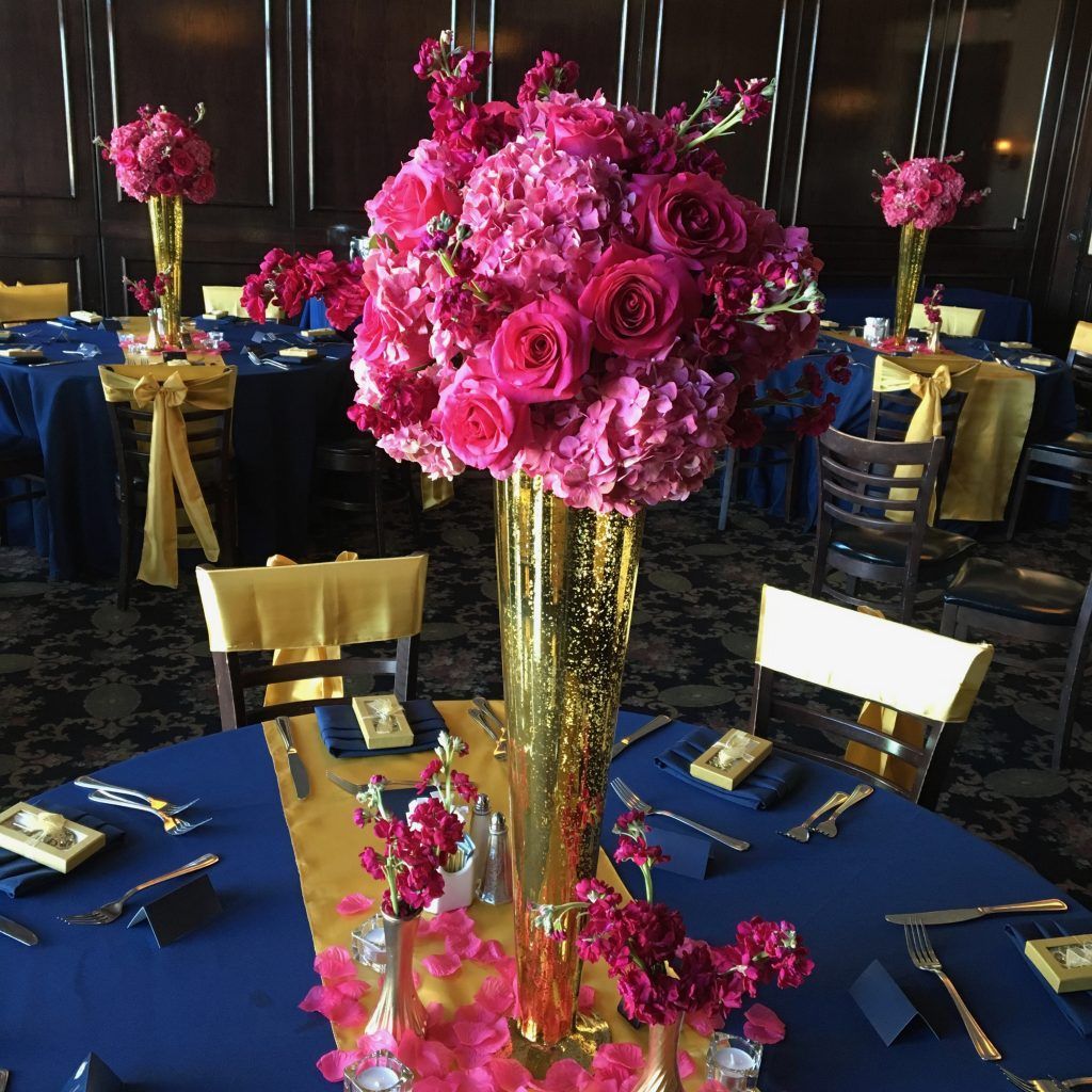 A gold vase filled with pink flowers sits on a table