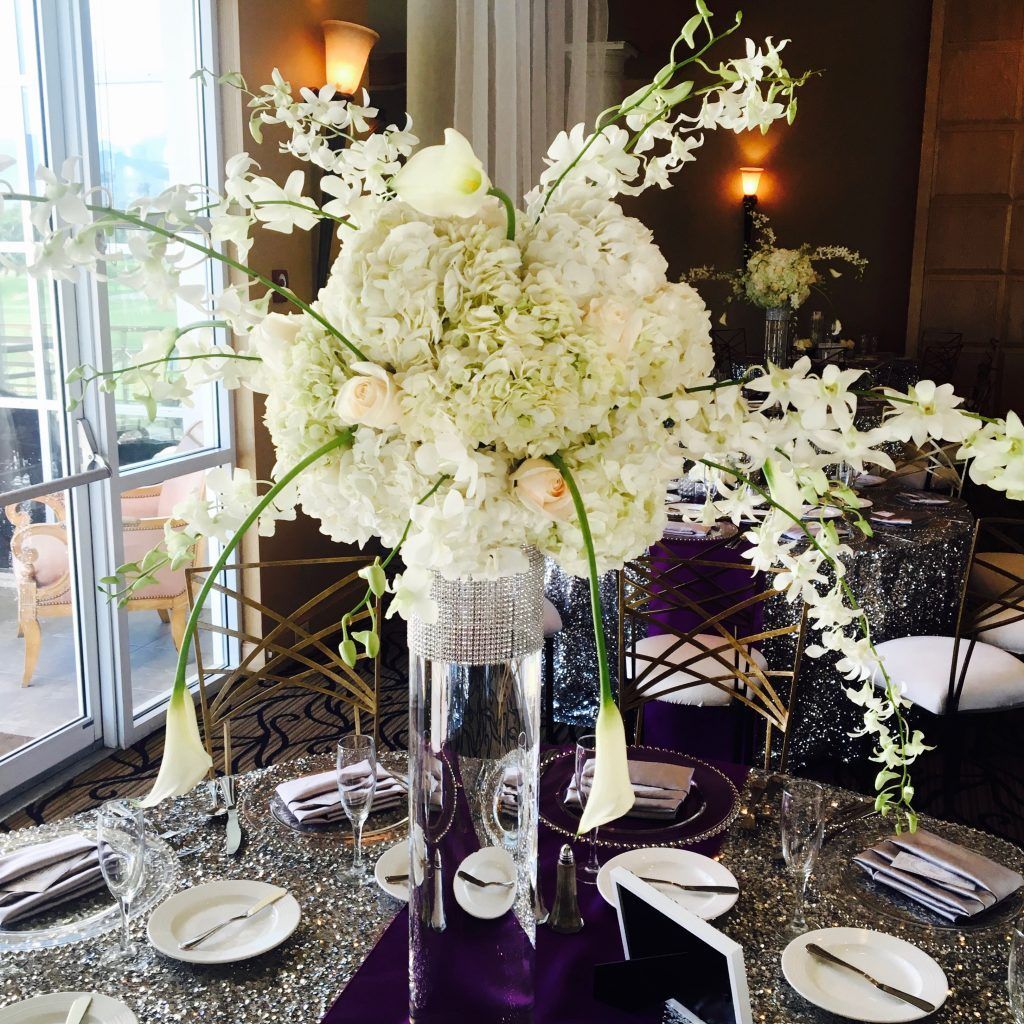 A tall vase filled with white flowers sits on a table
